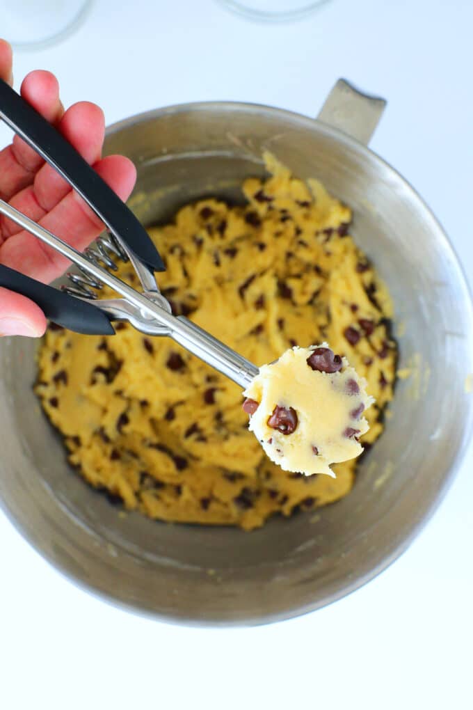 a hand holding a 1 tablespoon cookie scoop of dough over the bowl