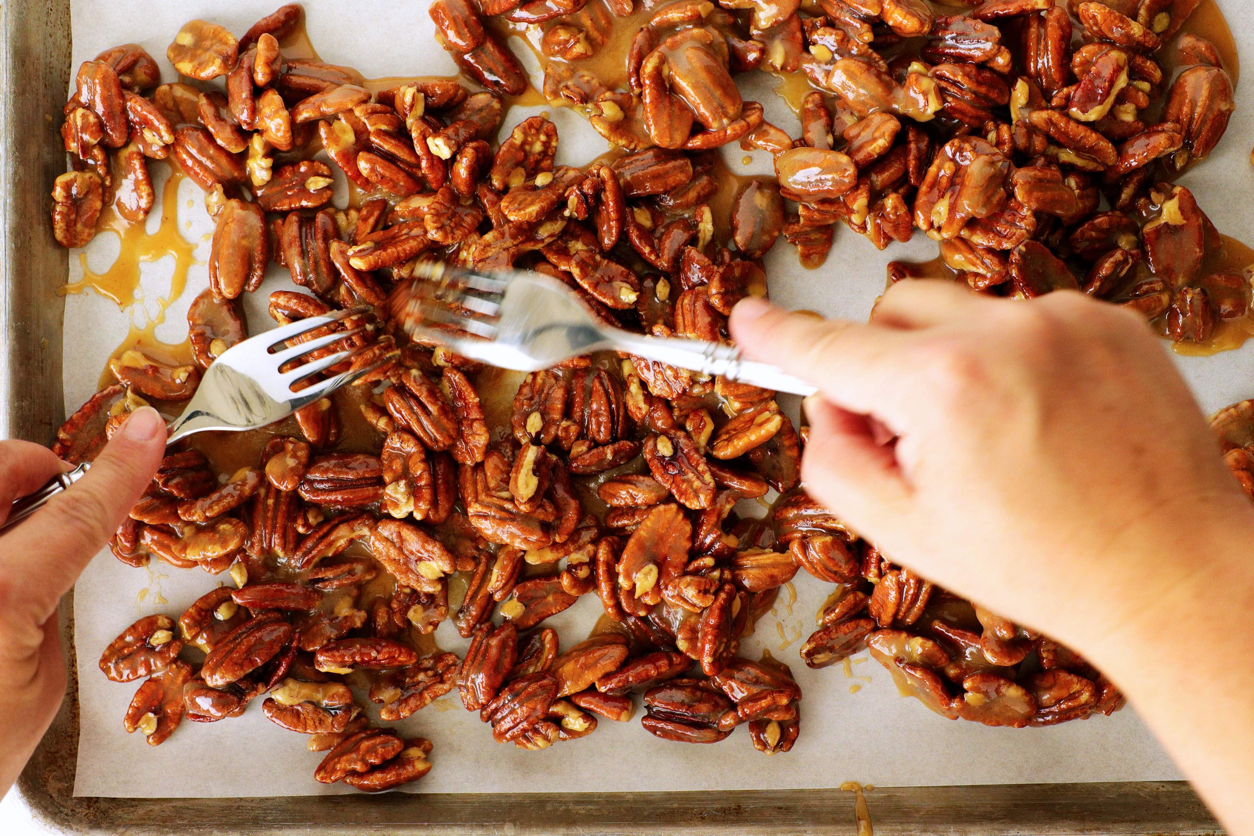 Two forks separating candied praline pecans on a lined baking sheet to cool