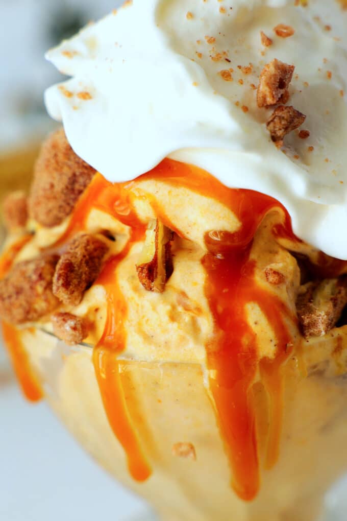 A close up of the ice cream in a glass dish with caramel drizzle, whipped cream, and candied pecans on top