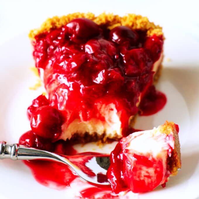 A close up of a slice of cherry cheesecake on a plate. the tip of the triangle piece is on a fork sitting with it