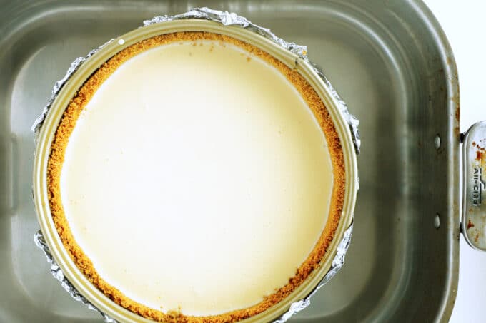an overhead view of an uncooked cheesecake sitting in a roasting pan