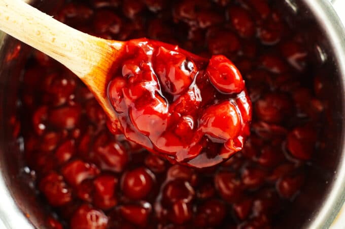 a spoonful of the thickened cherry topping lifted out of the pot, up toward the camera