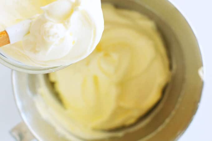 sour cream being added to the cream cheese/sugar mixture in the bowl of a stand mixer