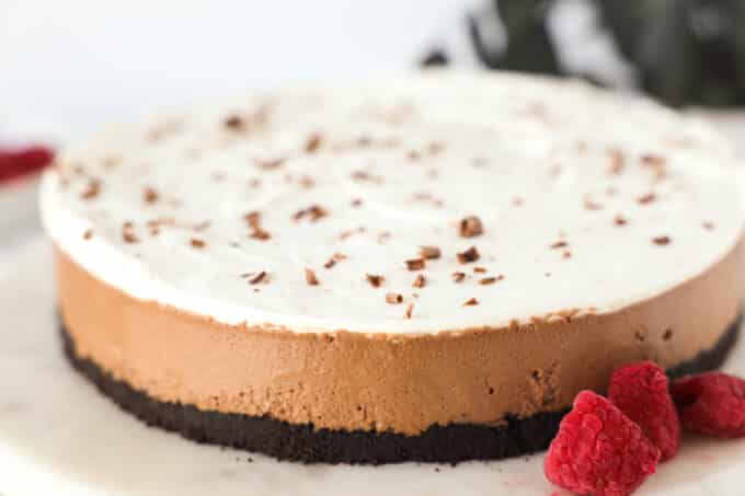 a whole chocolate mousse pie with chocolate shavings on top and raspberries on the side