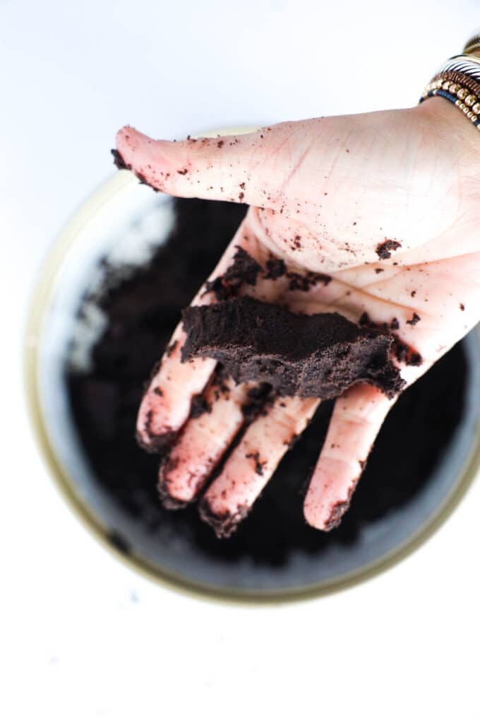 a hand holding a clump of damp Oreo cookie crumbs to demonstrate how it should hold together