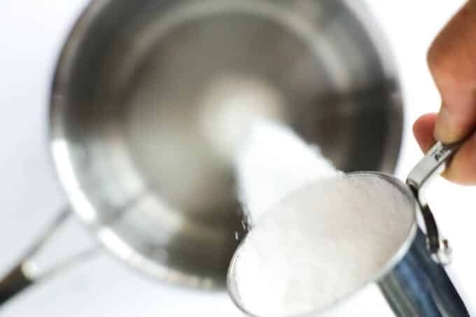 white sugar being poured from a measuring cup into a sauce pan