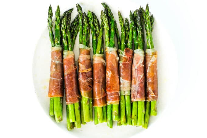 An overhead view of a row of prosciutto wrapped asparagus on a white plate