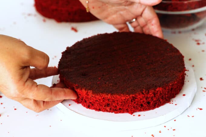 hands adjusting one layer of red velvet cake on a plate