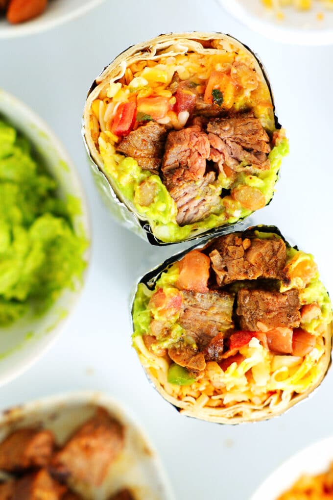 Two halves of a steak burrito standing on their ends to show the ingredients inside. Steak, cheese, rice, guacamole, and pico de Gallo are all visible
