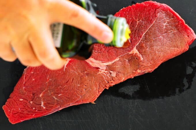 Avocado oil being drizzled over a raw steak