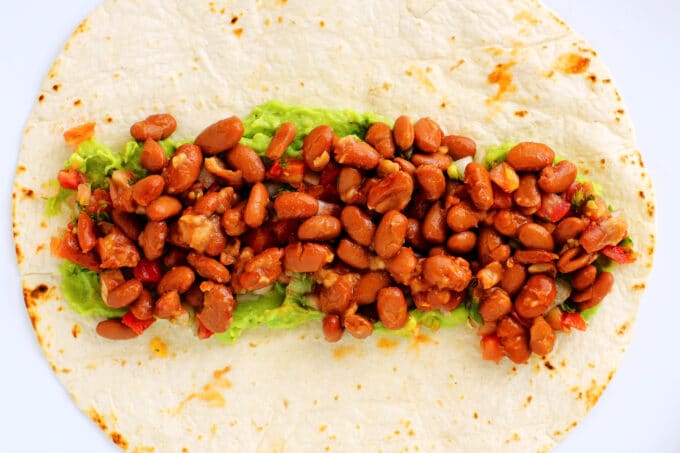 an overhead view of a flour tortilla with guacamole and beans on top