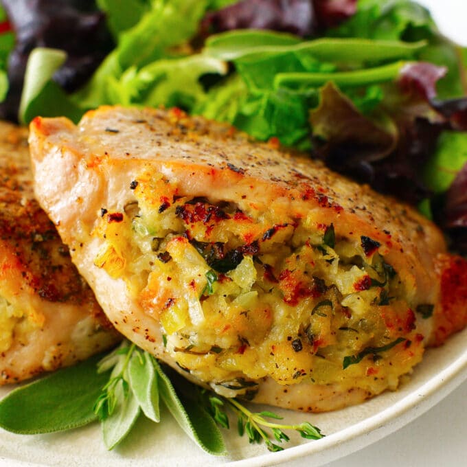 stuffed pork chops sit on a plate with salad behind it. one side of the chops are open and the stuffing is visible