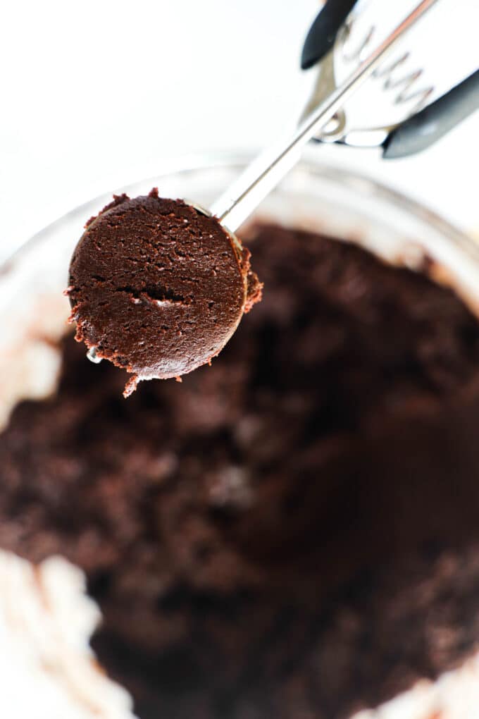 A tablespoon of chocolate cookie dough being held up to the camera above the bowl of cookie dough.
