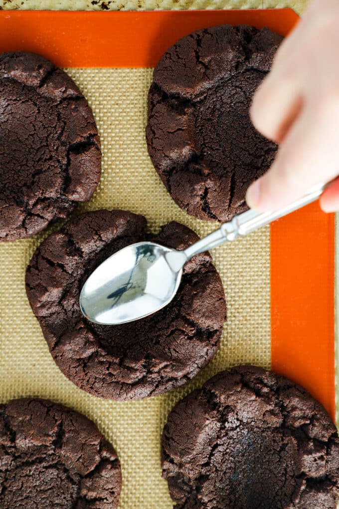 A spoon being used to make divots in the middle of freshly baked Andes Mint Cookies.