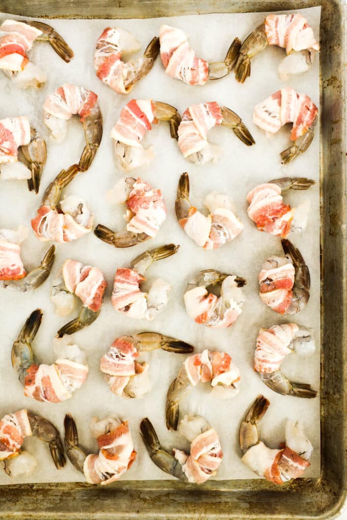 All of the shrimp wrapped in bacon, on a baking sheet and ready to cook.