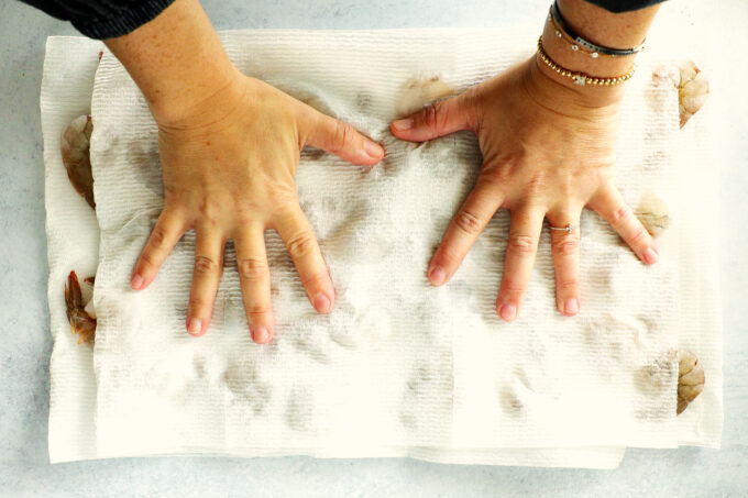 hands pressing down gently on shrimp covered with paper towels to remove moisture
