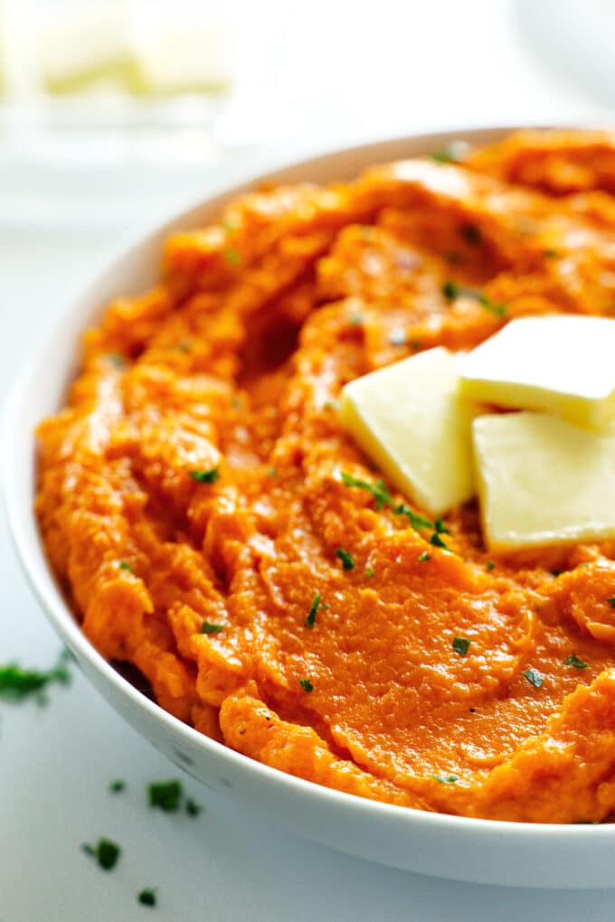 A close up of a bowl of Mashed Sweet Potatoes with butter and parsley on top.