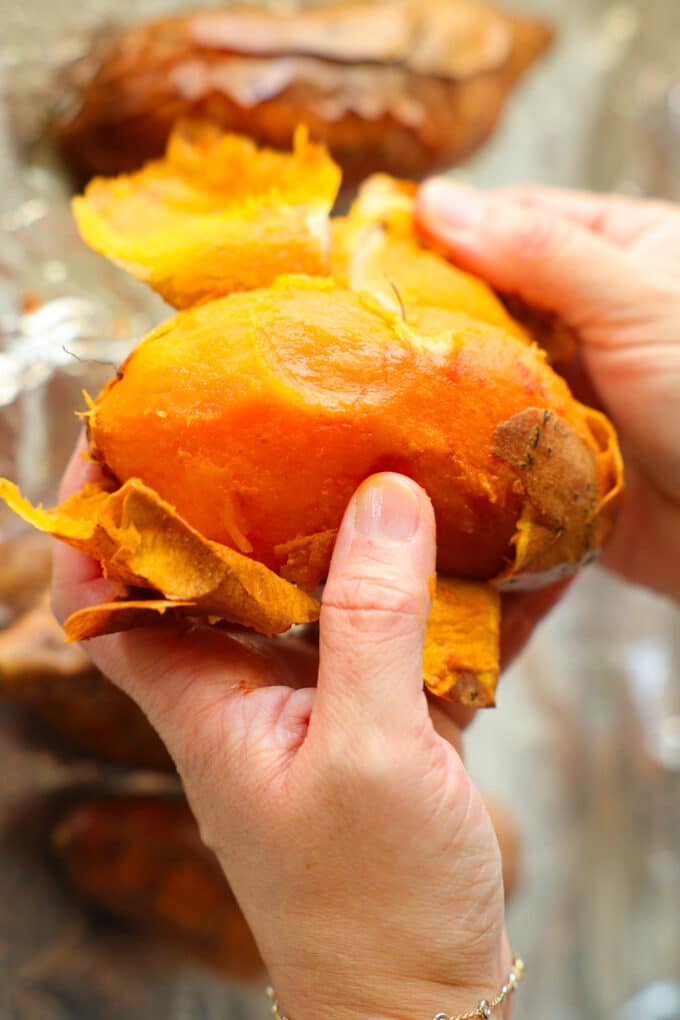 Hands peeling the skin off of a sweet potato.