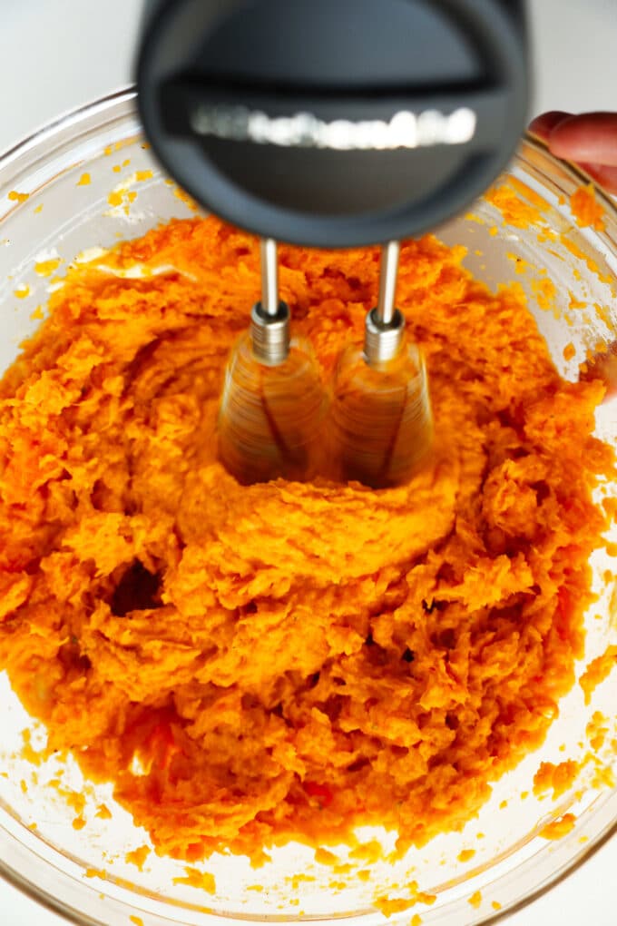 A hand mixer being used to blend sweet potatoes in a mixing bowl.