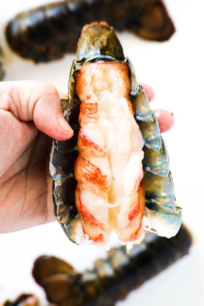 A hand holding a lobster tail with the shell pulled away, revealing the meat inside.