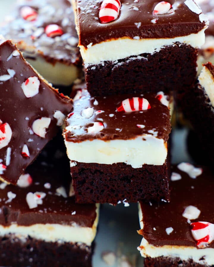 A close up of a stack of Peppermint Brownies with crushed peppermint candies on top. From the side the layers are very noticeable.