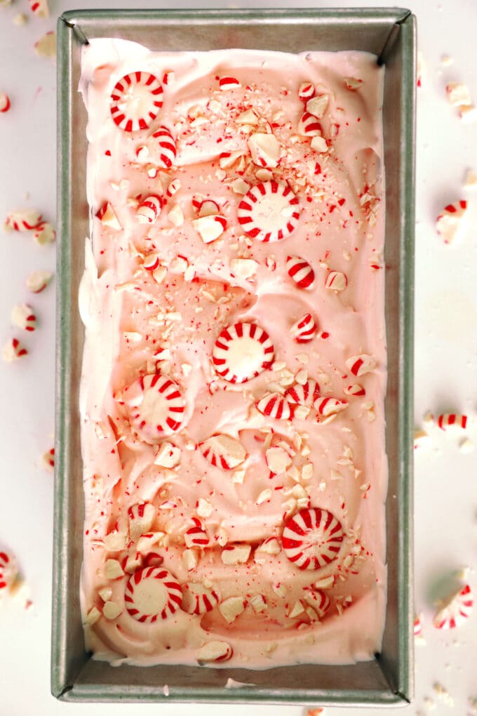 An overhead look at Peppermint Ice Cream in a loaf pan with peppermint candies scattered on top and over the counter around it.