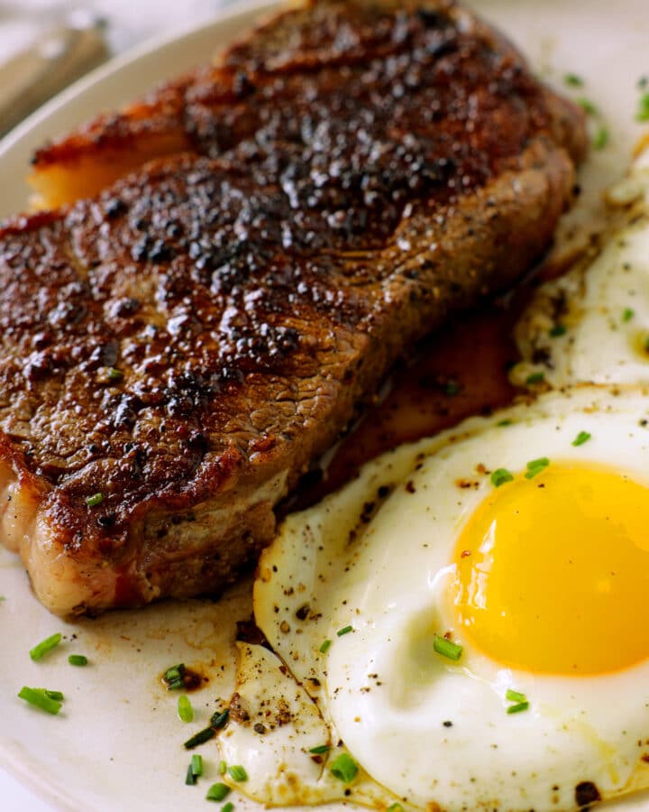 A close up of a plate of Steak and Eggs. The steak is tender and juicy and the eggs are sunny side up.
