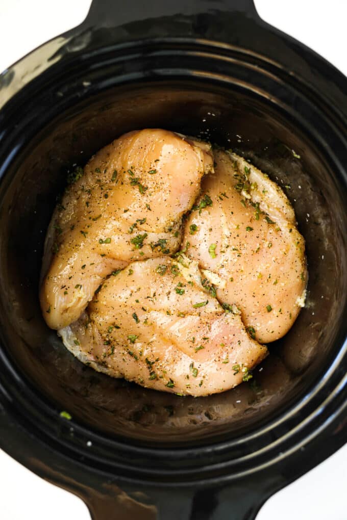 The raw chicken breasts in the crockpot with the herb and oil mixture rubbed all over them.