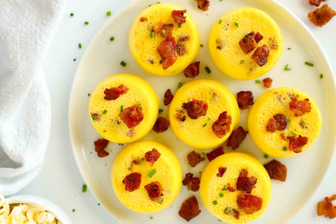 An overhead view of Egg Bites sitting on a white platter, pieces of cooked bacon sprinkled on top.