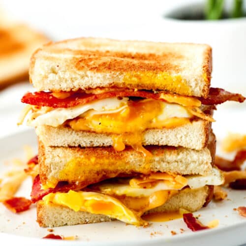 A close up of two halves of an Egg Sandwich stacked one on top of the other. You can see melty cheese, runny eggs, and crispy bacon.