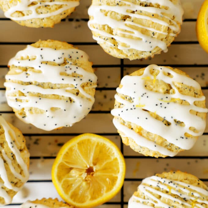 An overhead view of Lemon Poppy Seed Muffins on a cooling rack with half a lemon laying with them. The muffins are drizzled with a white glaze and sprinkled with poppy seeds.
