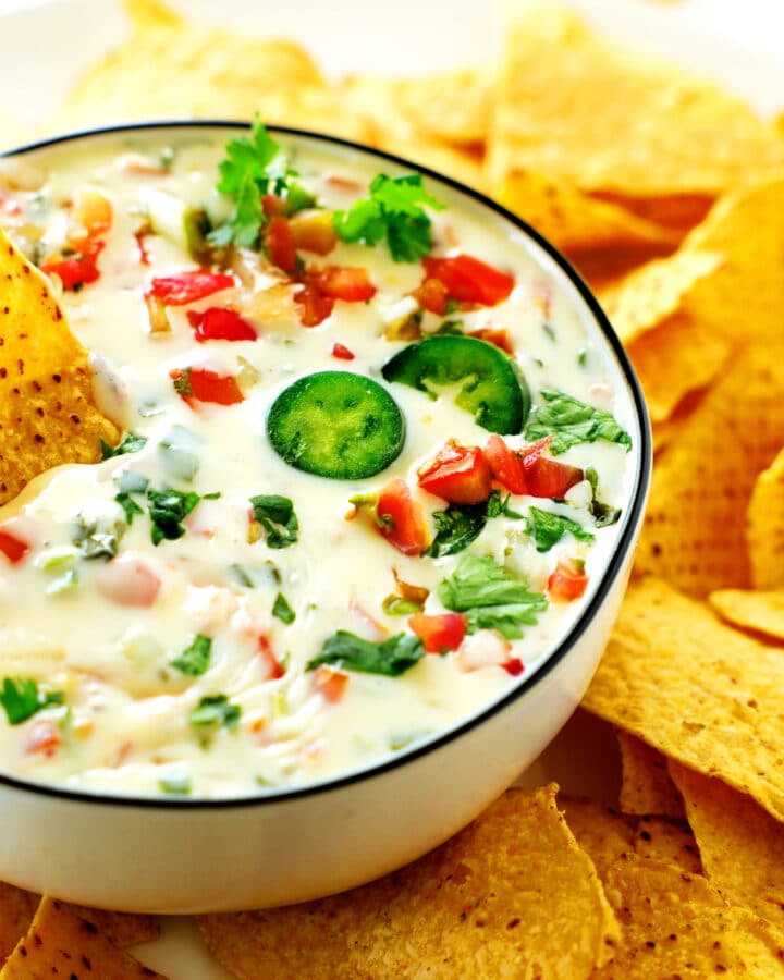 A bowl of Queso Blanco with jalapeño slices and cilantro on top and tortilla chips surrounding it.