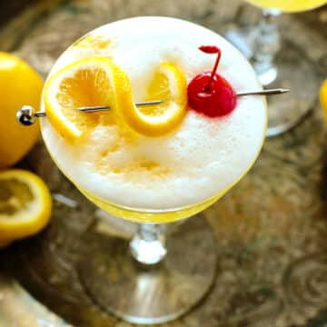 A Vodka Sour in a coupe glass with a lemon twist and cherry for garnish.