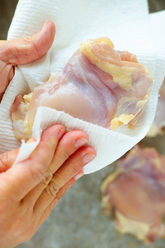 Hands using paper towels to pat raw chicken dry.