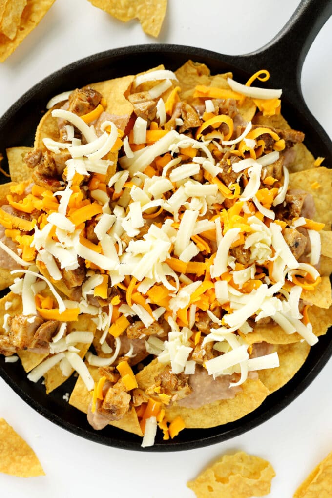 A pan of corn chips, refried beans, chicken, and cheese with more chips scattered around it.