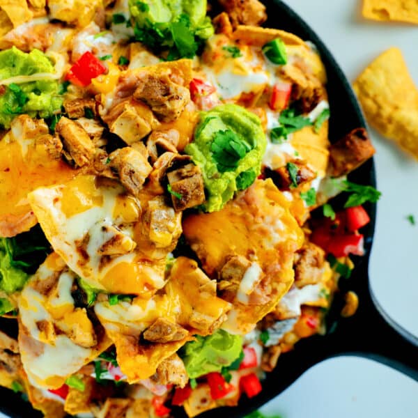 A close up of Chicken Nachos with guacamole and diced tomatoes on top.