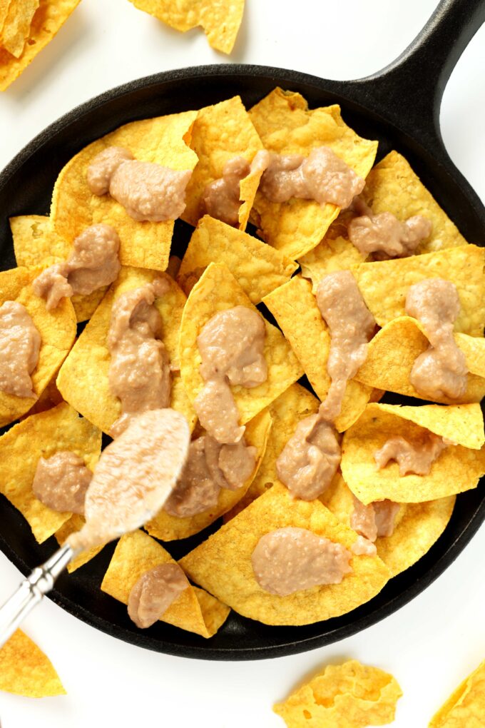 An overhead view of an iron pan with a layer of corn chips in the bottom and dollops of refried beans on top.