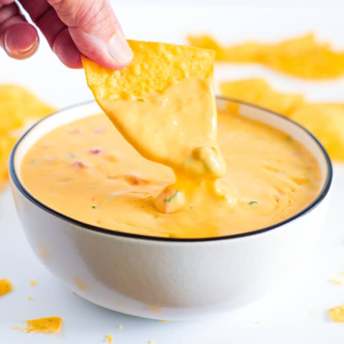 A close up of a tortilla chip being dipped into a bowl of Chile con Queso.