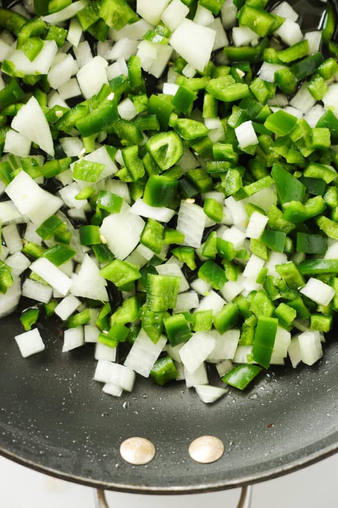 Raw, diced onion and jalapeños in a skillet.