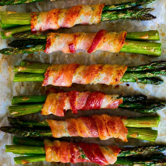 An overhead look at Asparagus Wrapped in Bacon bundles lined up on a sheet pan.