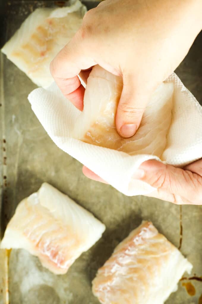 Hands using paper towels to pat the raw fish fillets dry.