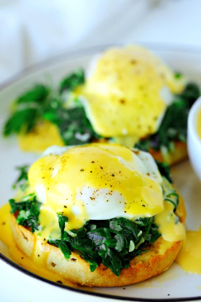 Eggs Florentine on a plate. There is a toasted English muffin with chopped, wilted spinach, poached eggs, and vibrant, yellow hollandaise sauce on top.