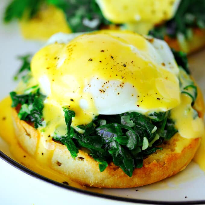 A close up of Eggs Florentine. There is a toasted English muffin with chopped, wilted spinach, a poached egg, and vibrant, yellow hollandaise sauce on top.