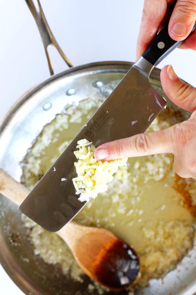 Minced garlic being slid off of the side of a knife into melted butter in a skillet.