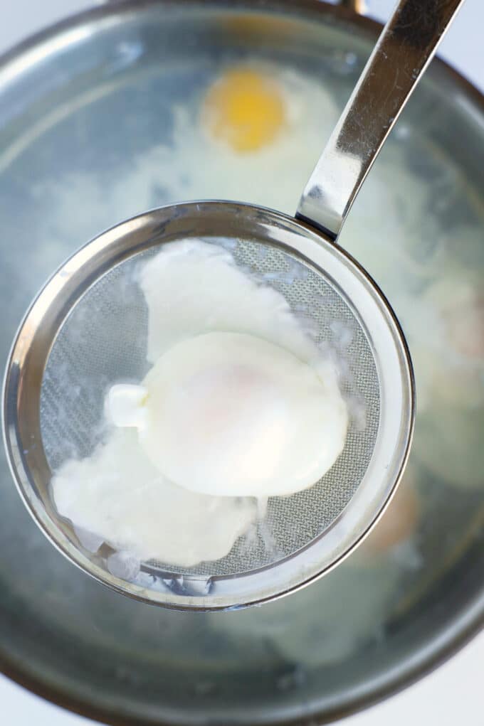 A poached egg lifted out of the water with a strainer.