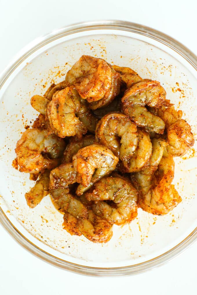 The raw, jumbo shrimp coated with oil and seasoning in a bowl.