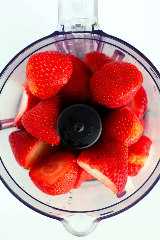 An overhead look into a blender of fresh strawberries with the tops cut off.