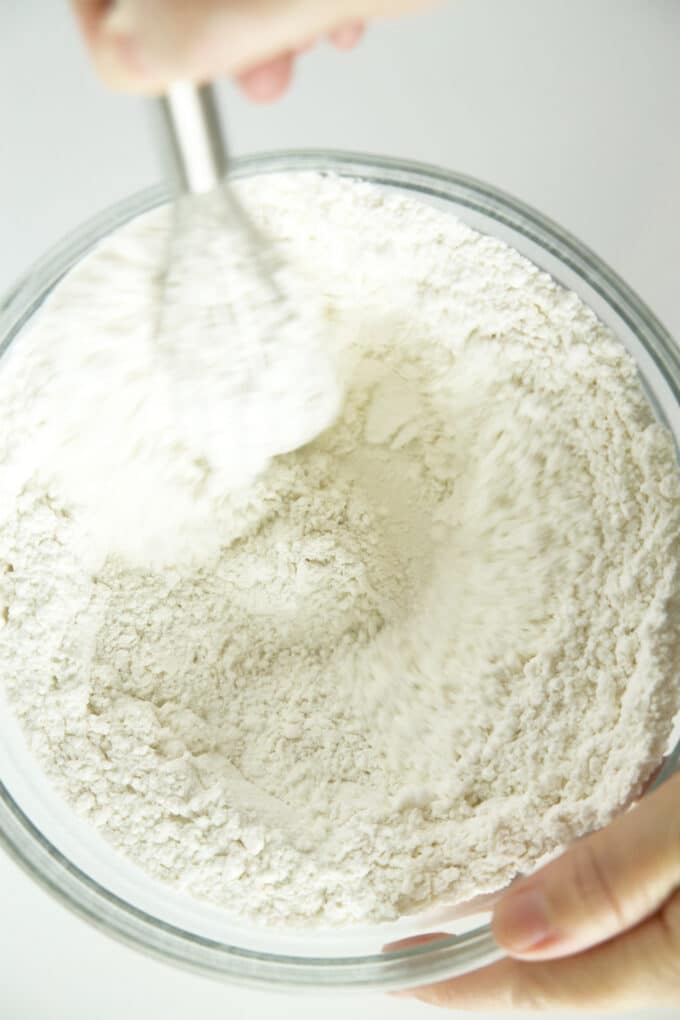 A person's hands whisking dry ingredients in a large bowl.