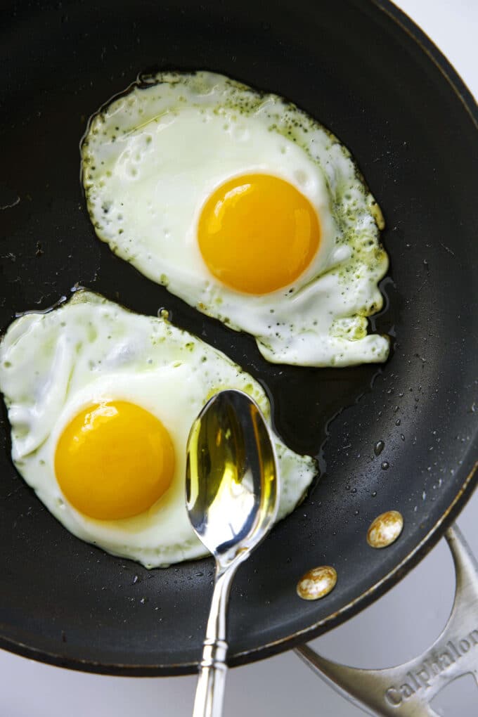 A spoon being used to scoop hot oil from the pan onto the whites of the Fried Eggs.