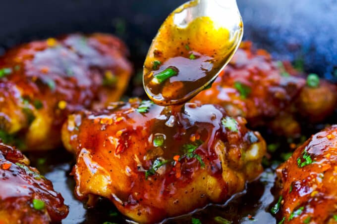 A spoonful of the honey garlic sauce is drizzled over the Honey Garlic Chicken Thighs, still in the skillet.